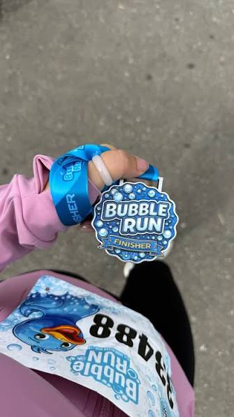 Runner holding a blue Bubble Run finisher medal on race day
